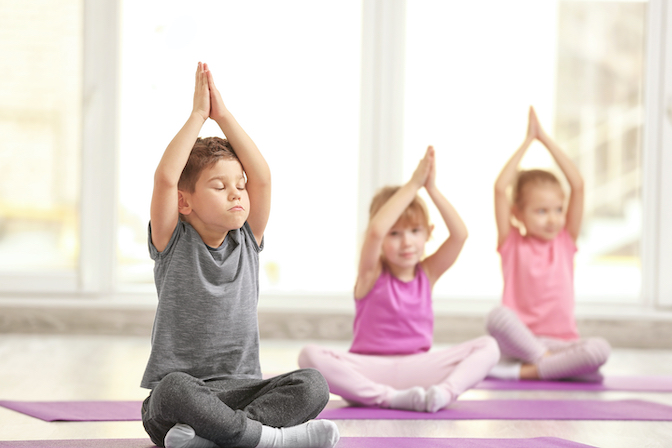 Ein kleiner Junge und zwei kleine Mädchen sind bei einer Stunde Yoga für Kinder