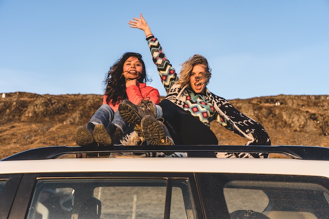 zwei junge Frauen sitzen auf dem Dach eines Autos - neue Leute kennenlernen