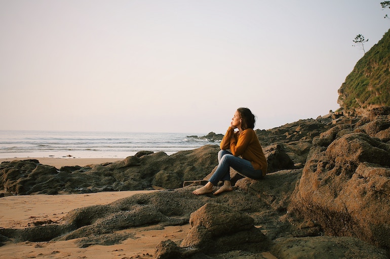 junge nachdenkliche Frau sitzt auf einem Fels - Unterbewusstsein