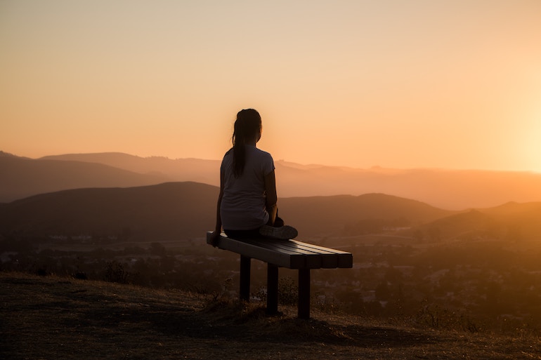 junge Frau sitzt auf der Bank und meditiert - erhöhtes Bewusstsein