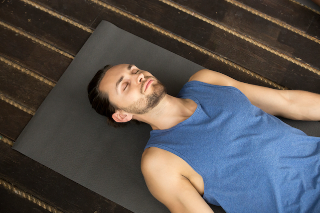 junger Yogi Mann liegt auf der Yoga Matte in Savasana - Yoga Nidra