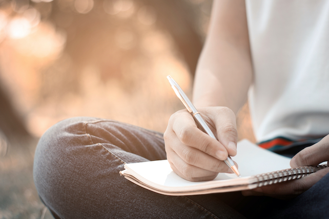 Tagebuch schreiben - Mensch sitzt im Schneidersitz und schreibt Tagebuch - Journaling