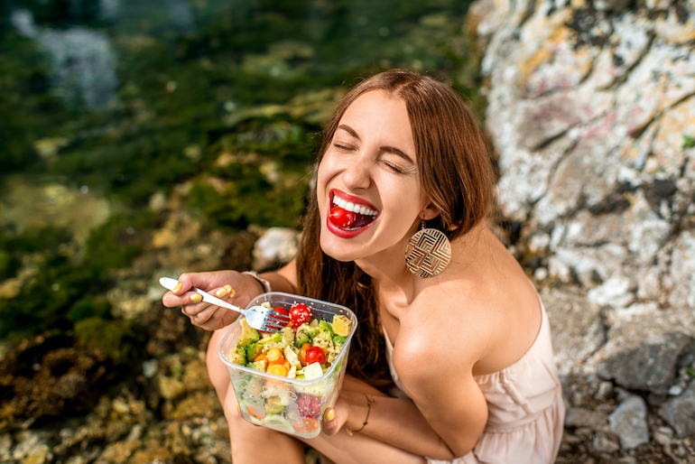 junge Frau lächelt und isst einen Salat - entzündungshemmende Lebensmittel