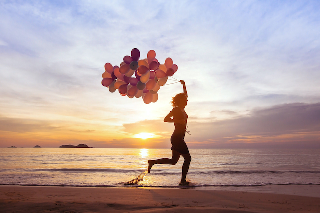 Sinn des Lebens finden und glücklich sein - Frau läuft mit vielen Luftballons in der Hand über den Sand am Meer