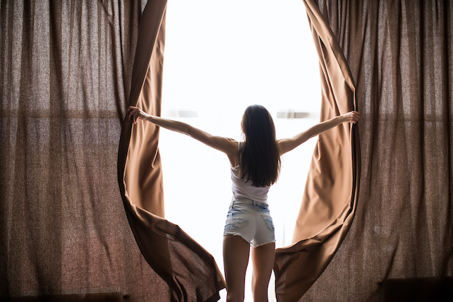 Hinteransicht junge Frau öffnet Morgens die Vorhänge - Morgenroutine