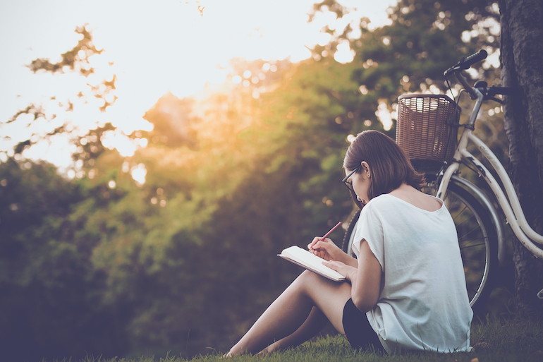 junge Frau sitzt in der Natur und ist am Tagebuch schreiben - Journaling