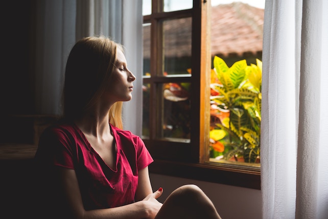 junge Frau mit geschlossenen Augen sitzt am Fenster und übt Achtsamkeit - Wege aus der Co Abhängigkeit