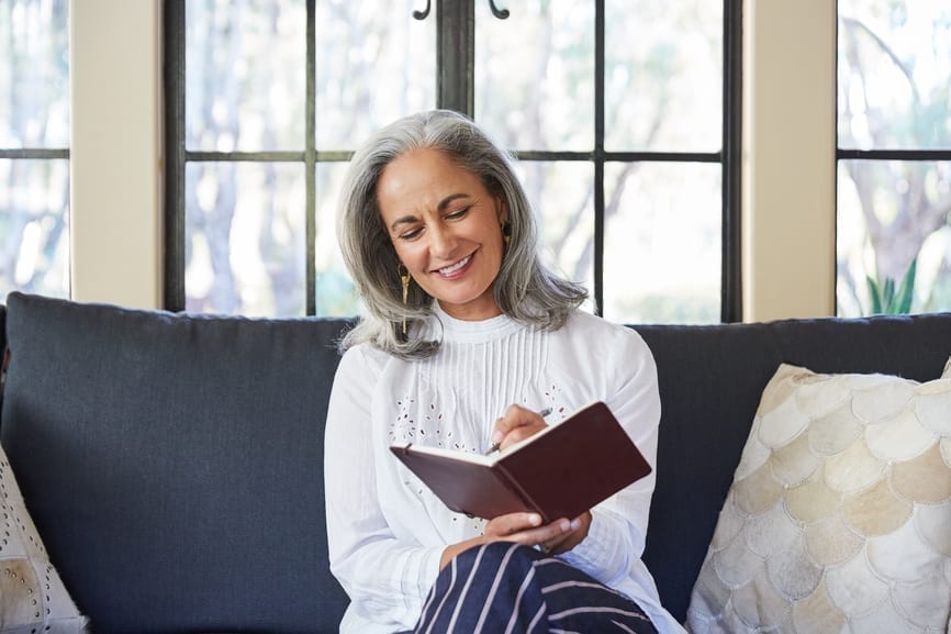 Mature Woman With Grey Hair Journaling In Living Room